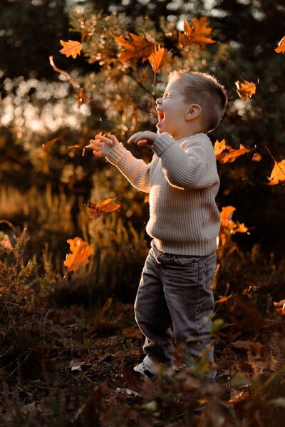 Jongen tijdens een gezinsshoot in de herfst die speelt met bladeren in Apeldoorn