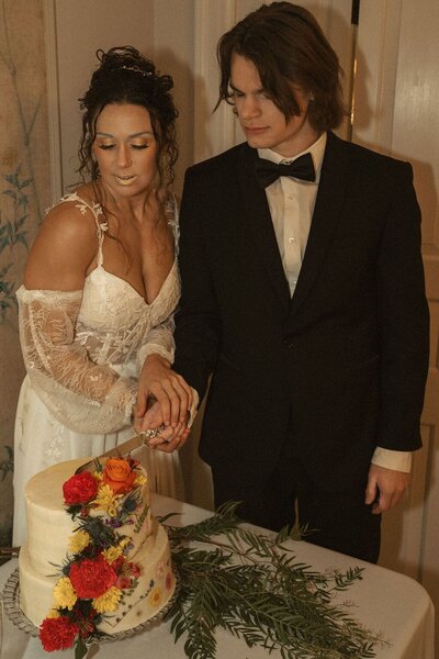 Bride and groom cutting floral-decorated wedding cake together at reception