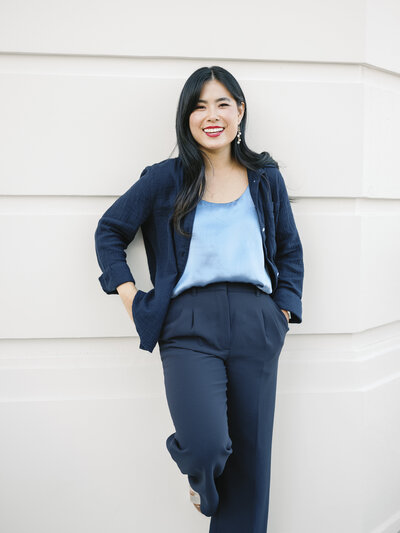 A woman standing and leaning on a white building in the city smiling at the camera during her brand session