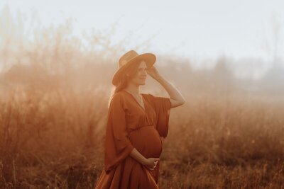 Zwangere vrouw met hoed in zacht licht van ondergaande zon


