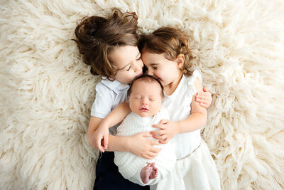 Big brother and big sister kiss their new baby brother.