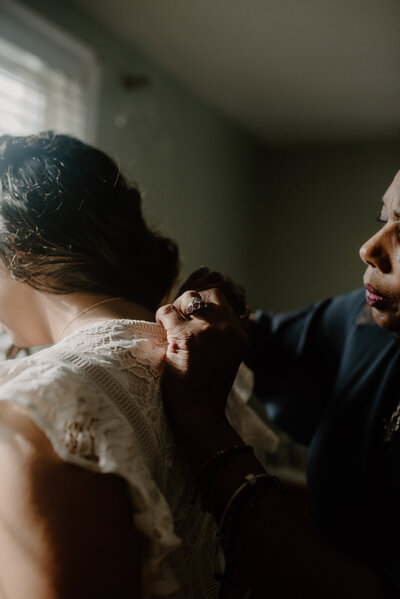 moody detail of intimate moment buttoning back of lace wedding dress getting ready