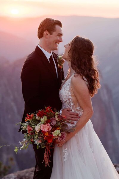 A bride and groom laugh while placing their custom wedding date stickers on their water bottles, while standing in view of Half Dome in Yosemite National Park. 