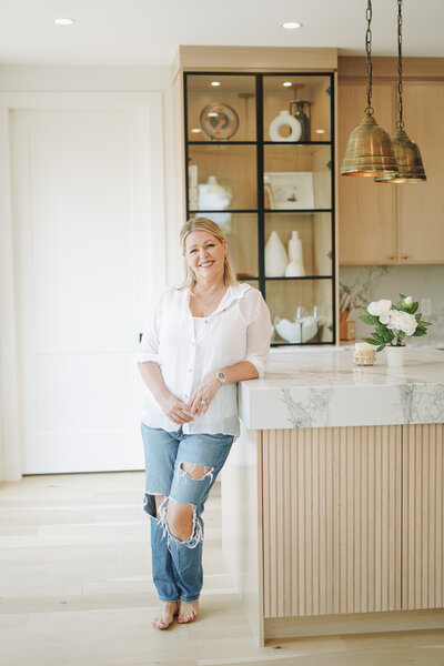 Melanie Greenough wearing a white shirt and jeans leaning against a counter