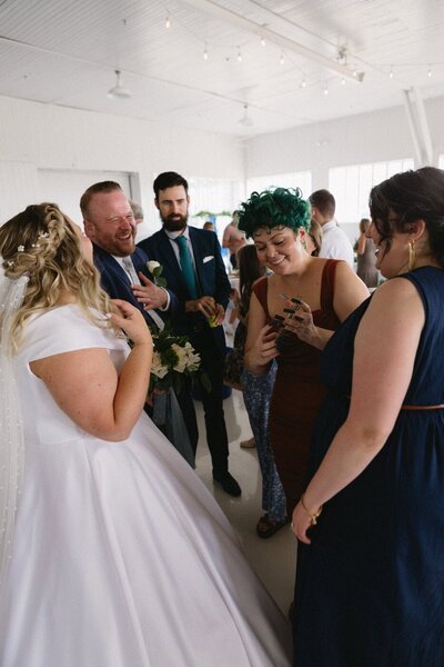 A wedding guest shares something on her phone as the bride and groom and other guests look on and laugh.