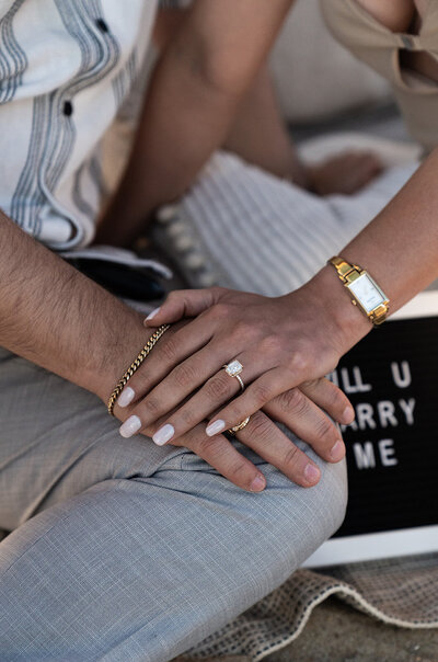 Close-up of a couple’s hands resting together, showcasing a sparkling engagement ring
