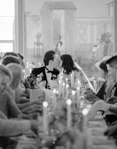 A couple kisses at their reception dinner with candles at the table