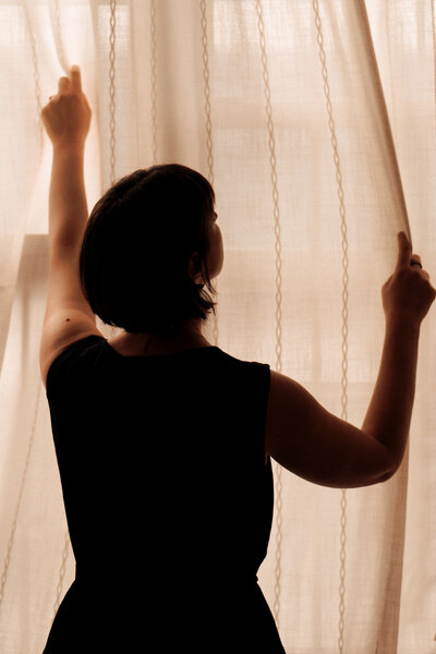 Silhouetted therapist parting curtains to let in light, symbolizing new beginnings, career growth, and somatic work in a Manhattan-based therapy practice.