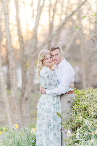 Newly engaged couple hugs close while standing in a garden at sunset
