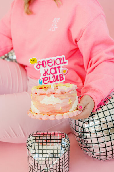 Kat Murphy in a pink Social Kat Media sweatshirt in front of a white wall