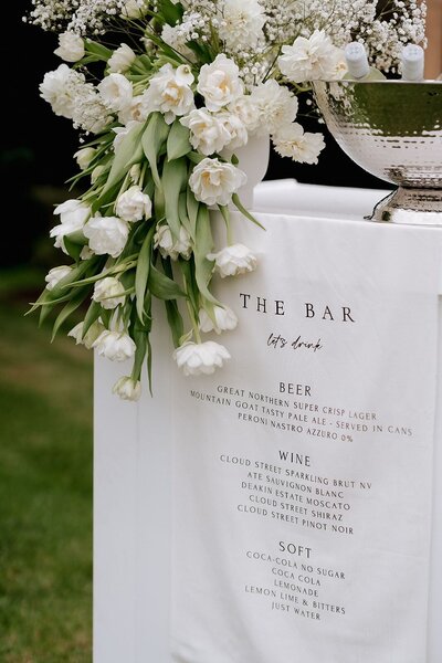 Large vase of green and white flowers on bar with drinks menu draping