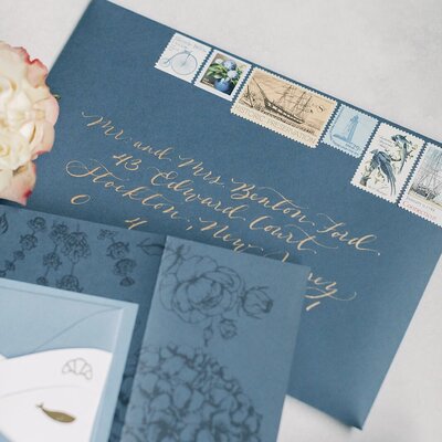 Black  wedding invitation envelopes with champagne ink calligraphy and vintage postage stamps.