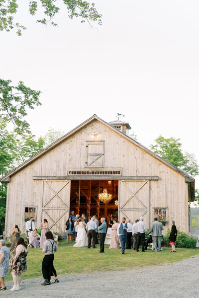 A gathering of people outside of a wedding reception in Vermont with a barn in the background.