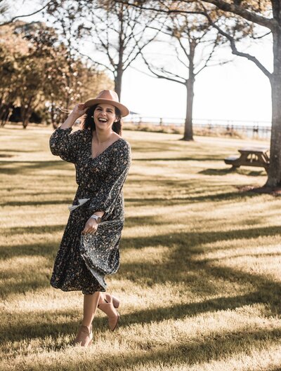 Katelin laughing with hat on a wind blown dress.