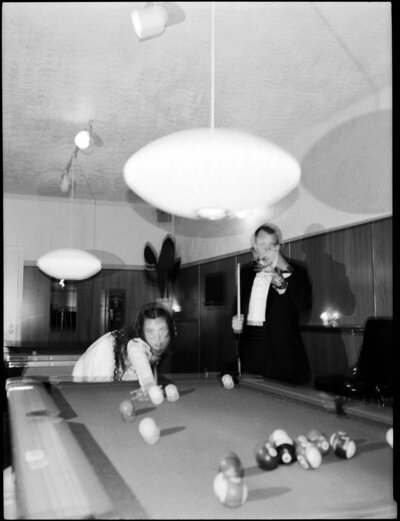 A blurry film photo of a bride and groom enjoying a game of pool in a cozy room.