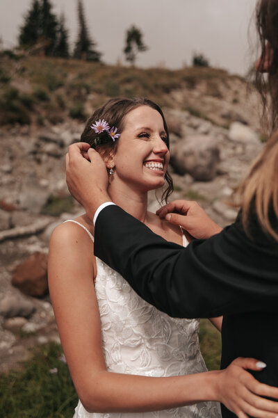 Groom tenderly tucking a wildflower behind the bride’s ear as they share a loving gaze, set against the rugged Mount Hood landscape near Portland, Oregon, captured in an intimate Pacific Northwest elopement photography session. 