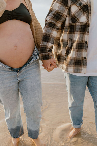 Photo of a couple holding hands at the beach, the mother is showing her pregnant belly