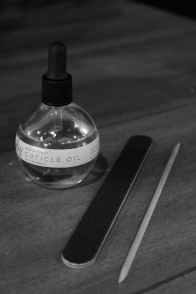 A bottle of cuticle oil next to a nail file and manicure stick in black and white