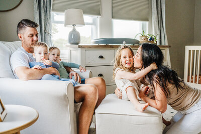 mom holds toddler daughters on lap and everyone laughs for a picture