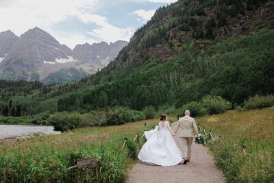 Bride and groom run along lakeside trail during Maroon Bells elopement.