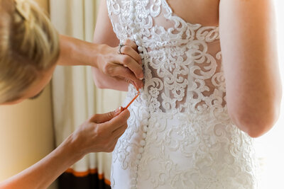 close up back of bride's dress, hands buttoning up bride's dress