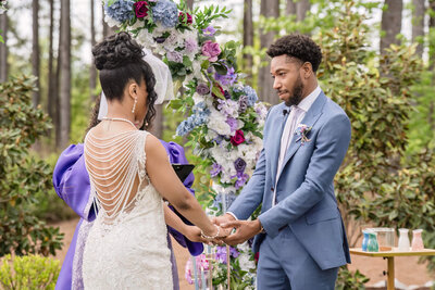 Romantic outdoor wedding ceremony as the bride and groom exchange vows under a floral arch.