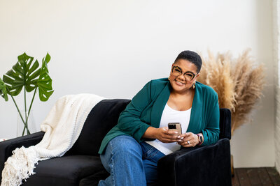 A professional woman dressed in a branded outfit, sitting gracefully on a grey couch, representing professional development for women and empowerment in career growth.