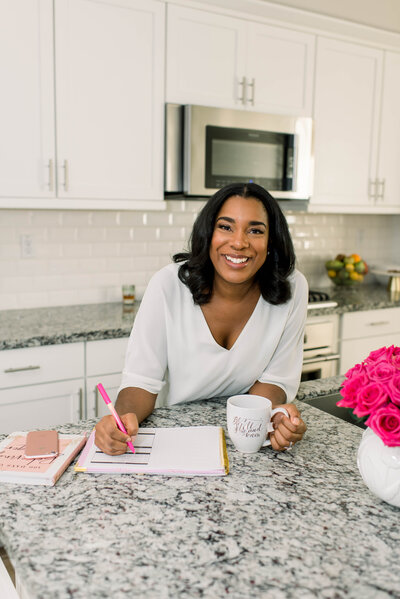 Woman leaning on kitchen counter and smiling while writing in planner