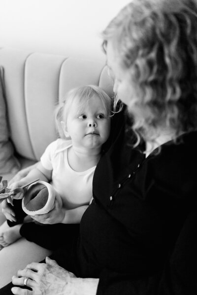 black and white image of toddler girl looking up at grandma while snuggling on a couch