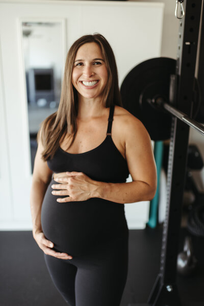 A mom holding her belly in a branding session at an in-home gym in Scottsdale