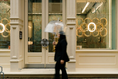 blurry image of woman holding an umbrella walking in front of a storefront window