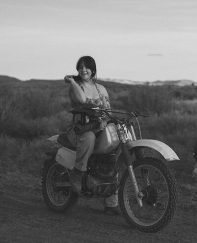 female photographer sitting on vintage motorcycle in the Oregon high desert during golden hour