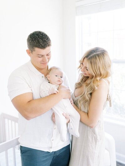 family of three smiling at baby boy while in his nursery