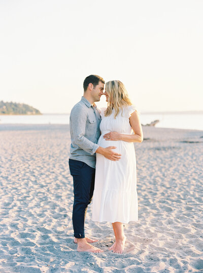 couple touching foreheads together during beach maternity photos
