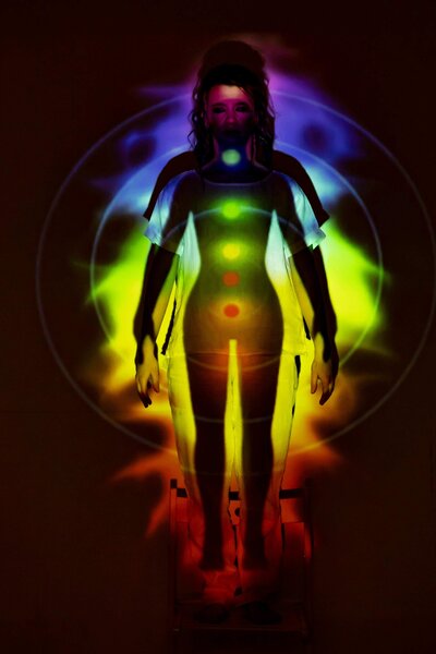 A woman standing with bright lights shining on her chakras 