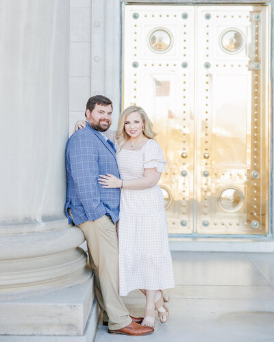 A happy couple snuggle on a column at the courthouse by a gold door