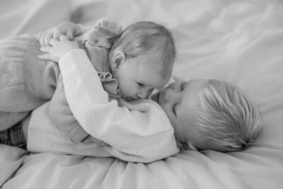 Baby and older brother lie on the bed in a close hug.