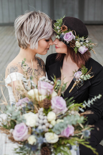 lesbian couple sitting next to each other  with their noses touching while holding a violet bouquet and one of the women wearing a violet flower crown in Knoxville TN