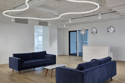 A spacious lounge area featuring deep blue couches, wood flooring, and a custom circular pendant light installation