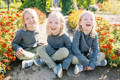 Photo of three young girls sitting and laughing in front of brightly colored flowers by Portland Family Photographer Emilie Phillipson Photography