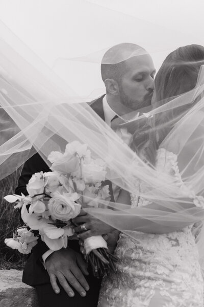 bride and groom kissing while bride's veil surrounds them