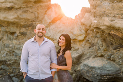 Engaged couple pose together for engagement session in front of large rocks at Table Rock Beach