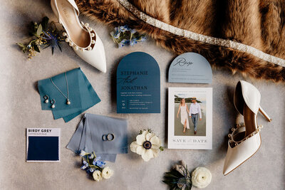 Flatlay displaying deep and slate blue stationery with winter wedding accessories