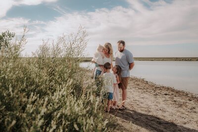 A man twirls his fiancée in a prairie field by a lake at sunset.