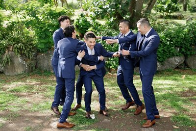 A wedding party laughing and hugging a newlywed 