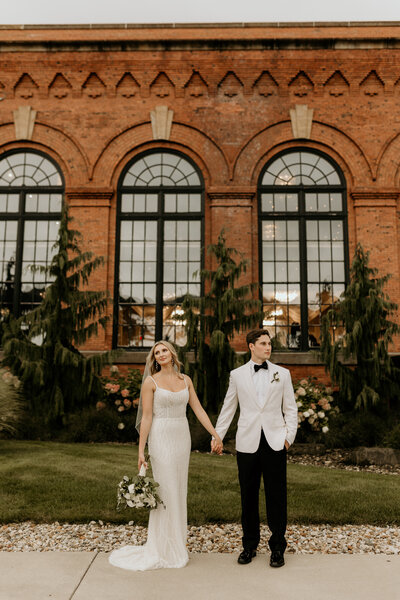 A newlywed couple holds hands outside of aesthetically pleasing windows