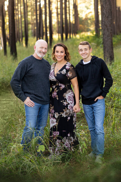 A picture of Spring, Texas photographer Bri Sullivan and her family are posing in the forest in Spring, Texas. They are dressed in casual clothes, smiling, and standing among trees and grass.