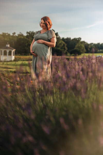 A man and woman stand together with eyes closed and touching foreheads. The woman is pregnant and they're both holding her belly. They're in a snowy field with mountains in the background for maternity pictures.