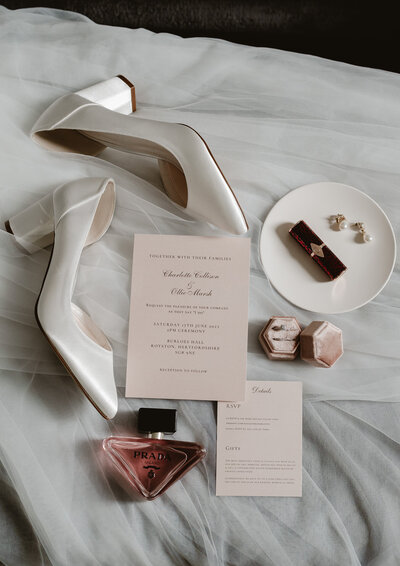 bride shoes, wedding invitations,  lipstick,pearl ear rings, rings and perfume sitting on vail