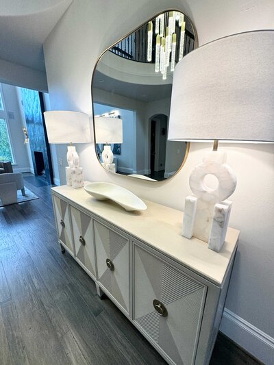 A white elegant desk in a residential interior design project in Frisco, featuring large lamps and a circular mirror.